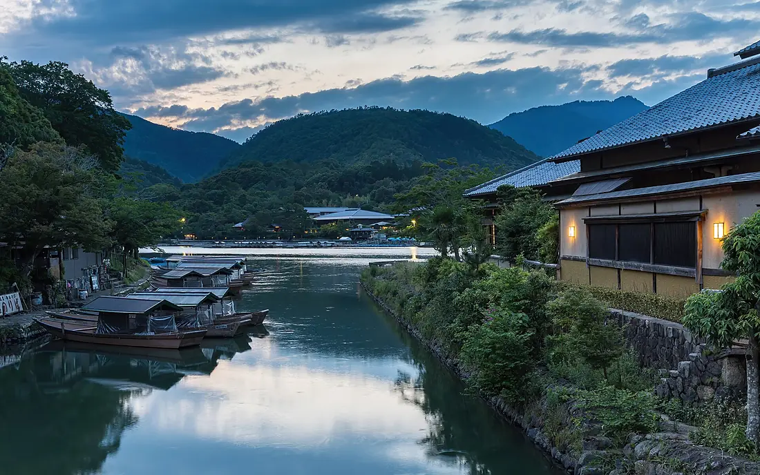 Katsura River bank with pleasure boats and illuminated building at sunset Kyoto Japan